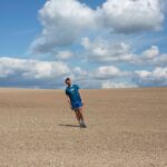 photographic image on a cloudy sunny day, there is a man standing at an angle in a big ploughed field.