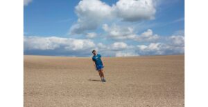 photographic image on a cloudy sunny day, there is a man standing at an angle in a big ploughed field.